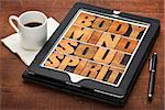 mind, body, soul and spirit - wellness concept - a collage of words in letterpress wood type on a digital tablet with cup of coffee