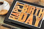 Happy birthday in letterpress wood type on digital tablet computer with stylus pen, coffee cup and cookie