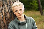 Close-up portrait of boy standing in front of tree in park, looking at camera, Germany