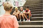 Backview of boy approaching girls sitting on stairs outdoors, Germany