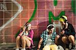 Children sitting next to wall outdoors, wearing headphones and listening to music, Germany