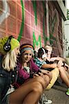 Group of children sitting next to wall outdoors, wearing headphones and listening to music, Germany