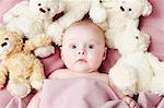 Baby girl lying surrounded by soft toys