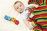 Baby boy lying under striped blanket with blocks spelling baby