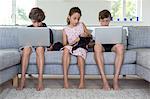 Brothers and sister on sofa with computers and knitting