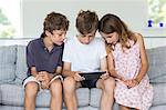 Brothers and sister on sofa looking at digital tablet