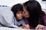 Mother kissing son on cheek in bed