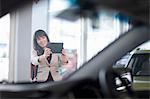 Mid adult woman photographing car in showroom