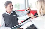 Car salesman handing keys to young woman in showroom