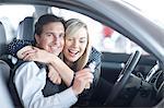Couple sitting in new car with key in showroom