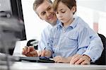 Boy sitting on father's lap using computer keyboard