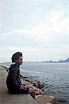 Young man sitting on wall looking at sea, Rio de Janeiro, Brazil