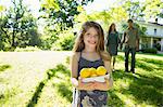 Farm. Children And Adults Working Together. A Girl Holding A Crate Of Lemons, Fresh Fruits. Two Adults In The Background.