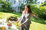 On The Farm. A Woman In A Farmhouse Garden, Preparing A Table With Fresh Organic Foods, Fresh Vegetables And Salads And Bowls Of Fresh Fruit, For A Meal.