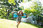 A Child Running Across The Lawn In Front Of A Farmhouse, Wearing Large Irridescent Blue Butterfly Wings And With Her Arms Outstretched.