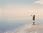 A Man Standing At Edge Of The Flooded Bonneville Salt Flats At Dusk, Taking A Photograph With A Smart Phone