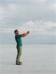 A Man Standing On Bonneville Salt Flats, Taking A Photograph With Tablet Device, At Dusk.