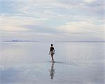 A Woman Standing On The Flooded Bonneville Salt Flats At Dusk. Reflections In The Shallow Water.