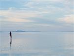 A Woman Standing On The Flooded Bonneville Salt Flats At Dusk. Reflections In The Shallow Water.