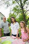 A Summer Family Gathering At A Farm. Three People Standing By A Table, Father And Daughters. Two Girls And A Mature Man.