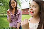 Family Party. A Child With A Fresh Cherry Between Her Teeth. A Young Woman Watching Her And Laughing.