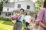 Family Party. Parents And Children Walking Across The Lawn Carrying Flowers, Fresh Picked Vegetables And Fruits. Preparing For A Party.