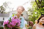 Family Party. A Woman Carrying A Large Bunch Of Rhododendron Flowers, Smiling Broadly.