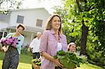 Family Party. Parents And Children Walking Across The Lawn Carrying Flowers, Fresh Picked Vegetables And Fruits. Preparing For A Party.