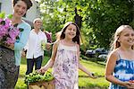 Family Party. Parents And Children Walking Across The Lawn Carrying Flowers, Fresh Picked Vegetables And Fruits. Preparing For A Party.