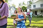 Family Party. Parents And Children Walking Across The Lawn Carrying Flowers, Fresh Picked Vegetables And Fruits. Preparing For A Party.