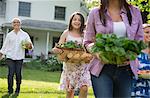 Family Party. Parents And Children Walking Across The Lawn Carrying Flowers, Fresh Picked Vegetables And Fruits. Preparing For A Party.