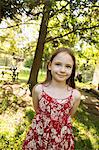 A Young Girl In A Red Floral Summer Dress In The Shade Of Trees.