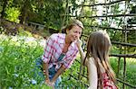 A Mother And Daughter Together In A Plant Enclosure In A Garden. Green Leafy Plants. A Child Touching The Adult Woman's Nose.