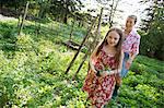 A Young Girl Holding A Seedling Plant, And Walking Through The Gardens Of The Farm With An Adult Woman Following.