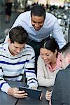 Business People On The Move. Four People Gathered Around A Digital Tablet Having A Discussion. Overhead View.