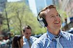 A Man Listening To Music On His Headphones. A Couple In The Background.