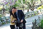 A Man In A Business Suit Astride A Bicycle. A Woman Kissing Him Goodbye.