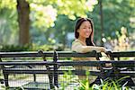 A Woman Sitting In A City Park On A Bench In The Sunshine.