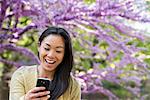 A Woman Sitting In A Park Looking At Her Smart Phone And Laughing.