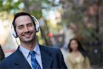 A Man In A Business Suit Wearing White Headphones, Listening To Music.