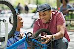 A Family In The Park On A Sunny Day. A Father And Son Repairing A Bicycle.