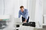 Business. A Man Standing Over A Desk, Leaning Down To Use A Laptop Computer.