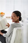 Business. A Woman Sitting And Reading A Book. Research Or Relaxation. Looking Over Her Shoulder And Smiling.