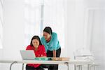 Business. Two Women Leaning Over And Using A Laptop Computer.