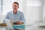 Business. A Light Airy Office Environment. A Man Sitting Holding A Digital Tablet.