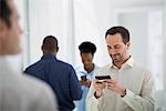 Office Interior. A Group Of People, One Man Using A Smart Phone.