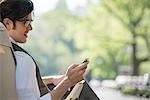 City Life. A Man Sitting In A Canvas Camping Chair In The Park Looking At His Cell Phone.