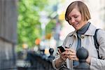 City. A Woman In A Jacket Checking Her Smart Phone.