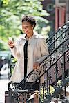 City. A Woman On Steps Outside A Town House, Checking Her Smart Phone.