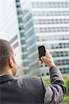 City. A Man In A Business Suit Holding His Smart Phone At Arms Length.